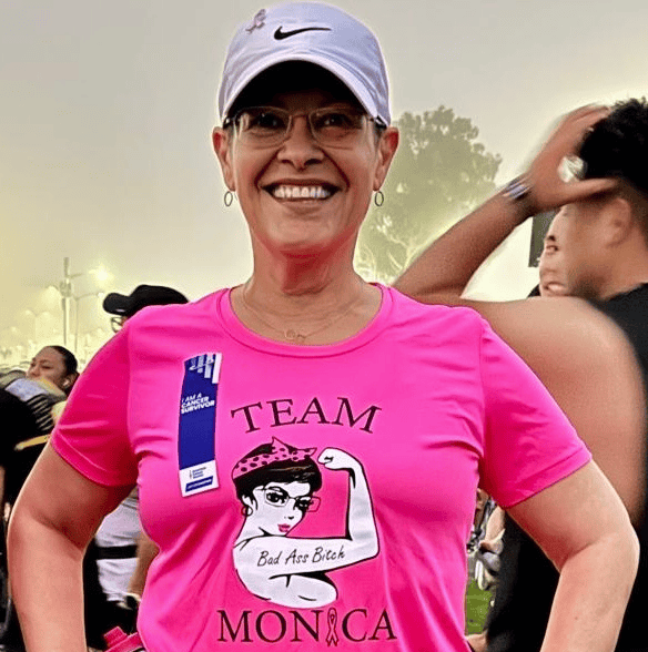 Breast cancer survivor Monica is wearing running gear and Team Monica Race shirt, smiling. 